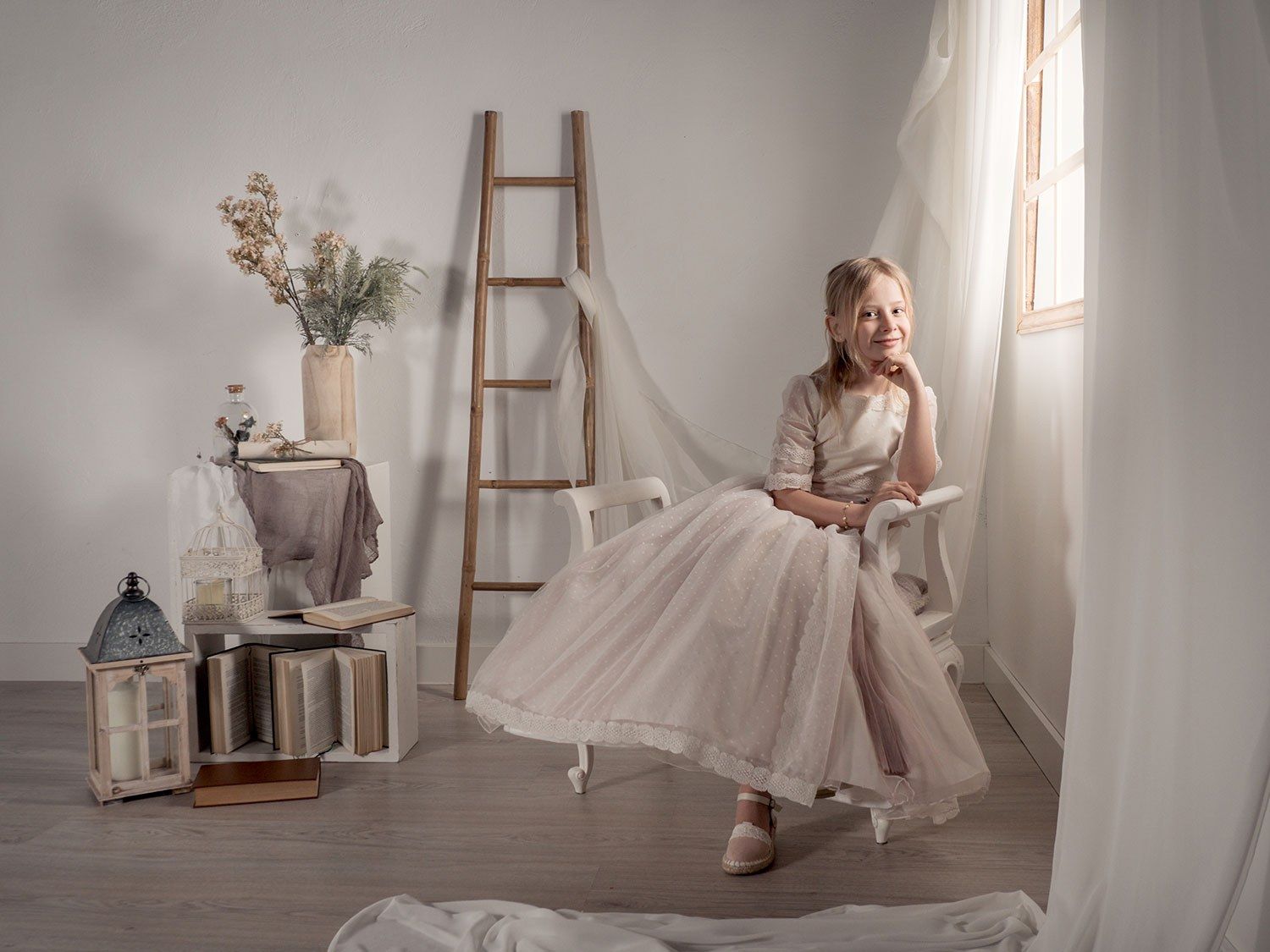 Una niña con su vestido de comunión, sentada junto a una ventana
